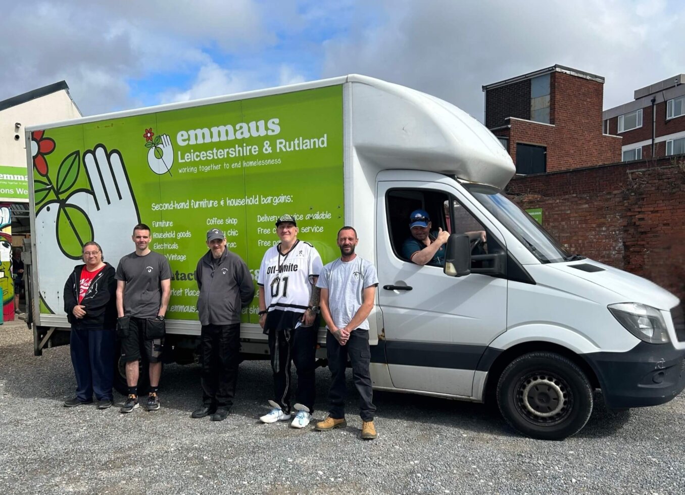 Group from Emmaus standing smiling, in front of Emmaus van. Emporium shop visible in background.