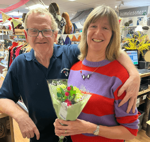 A male companion hands a bunch of flowers to a female shopper. They are both happy and smiling at the camera.