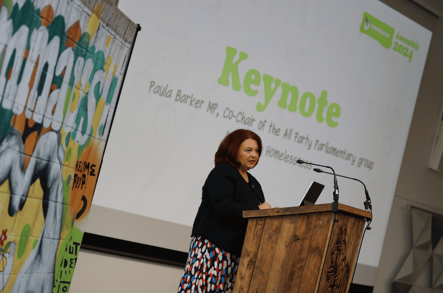Paula Barker MP, standing at a podium, making a speech at Emmaus Assembly 2024
